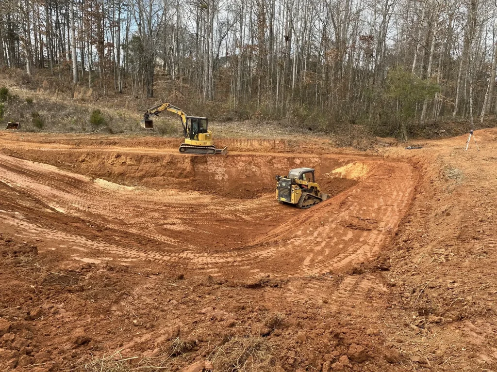 Better Way Land Management LLC excavator and skid steer clearing red clay terrain with bare winter trees in background