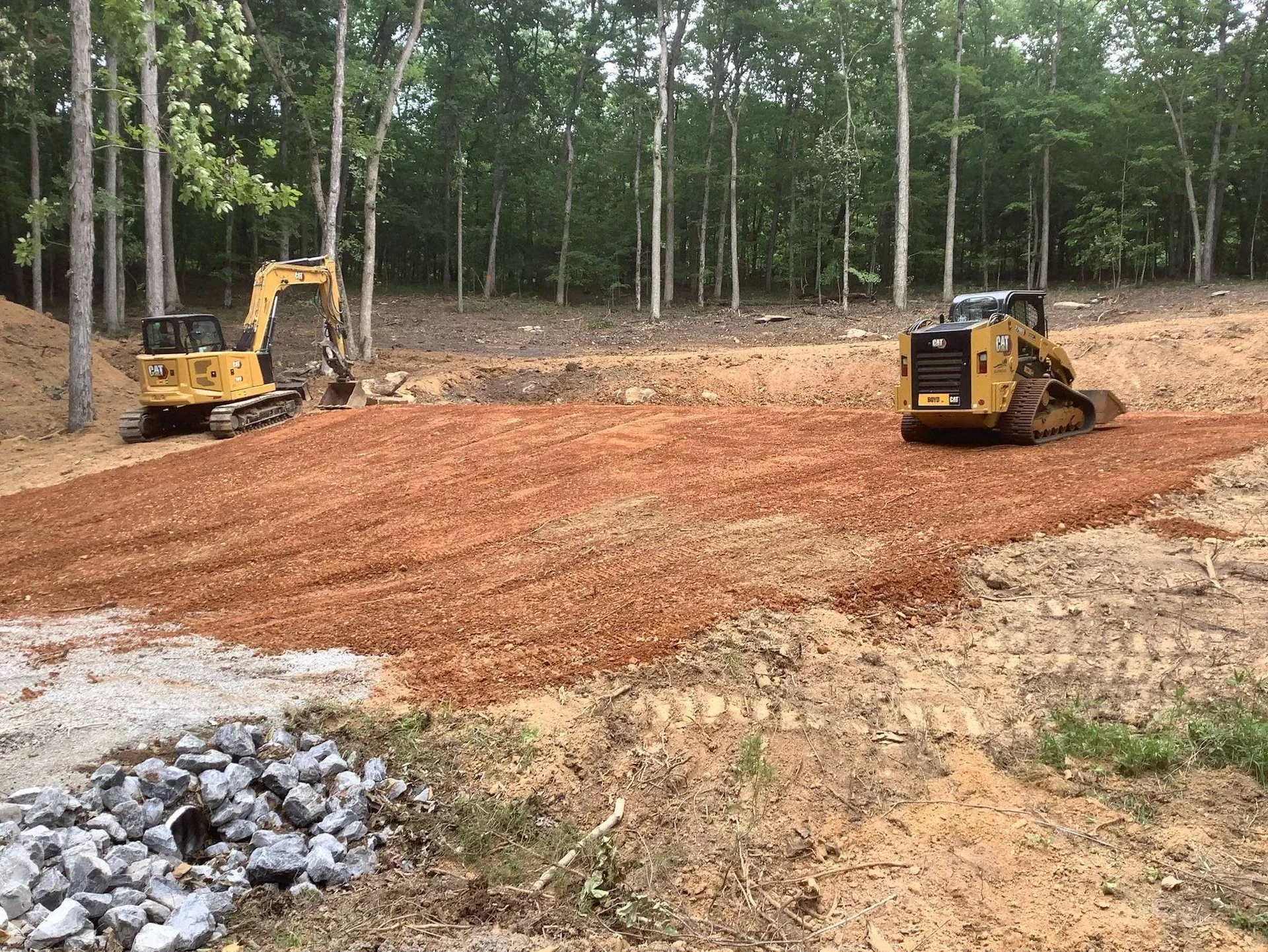 Better Way Land Management LLC CAT excavator and skid steer grading red clay soil on cleared wooded lot in OH